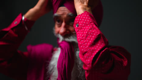 Primer-Plano,-Toma-De-Estudio-Con-Iluminación-Tenue-De-Un-Hombre-Sikh-Mayor-Con-Barba-Atando-Una-Tela-Para-Un-Turbante-Contra-Un-Fondo-Oscuro,-Filmado-En-Tiempo-Real